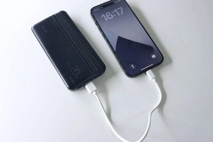 黒いモバイルバッテリーとスマートフォンが白い充電ケーブルで接続され充電中