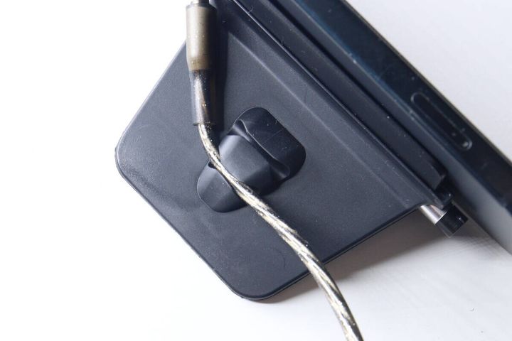 黒いスマホスタンドの背面にあるコードクリップに、充電ケーブルが挟まれている様子。