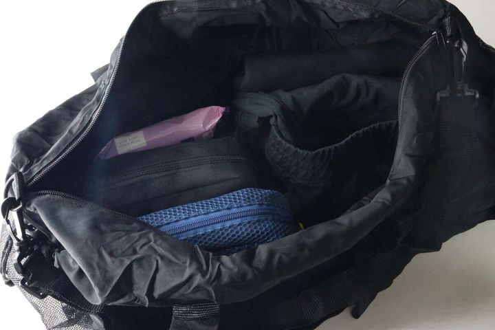 黒いバッグのメイン収納部が開けられ、衣類やポーチが詰め込まれている