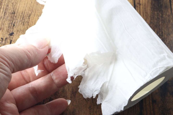 指で圧縮トイレットペーパーの端を剥がそうとしているが、紙が崩れてしまっている様子。