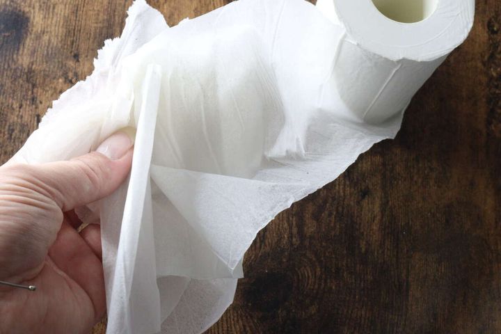 指で圧縮トイレットペーパーの紙を重ねて持ち、柔らかさを確認している様子。