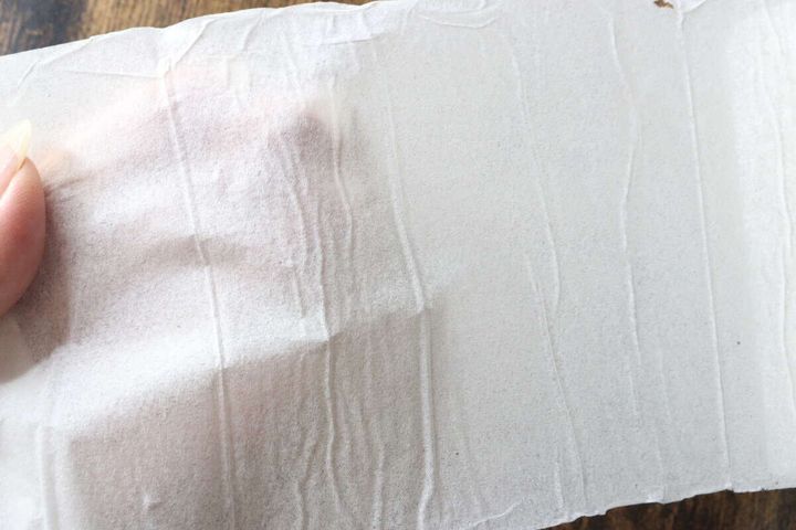 指で広げられた圧縮トイレットペーパーの紙が薄く透けている様子。