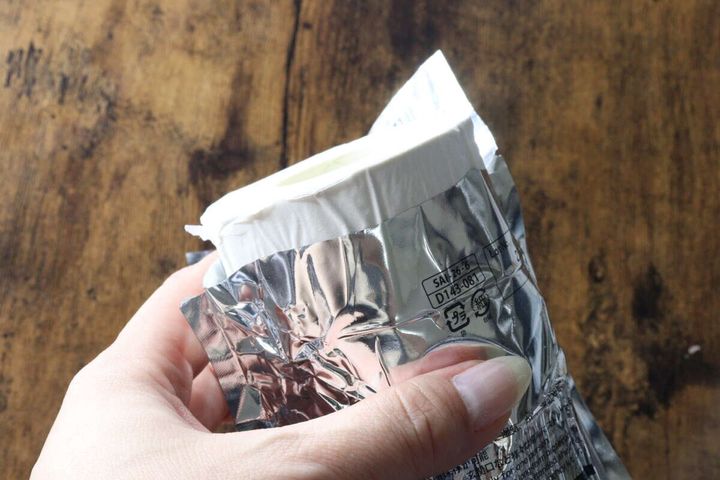 指でアルミ包装を剥がし、中から白い圧縮トイレットペーパーを取り出している様子。