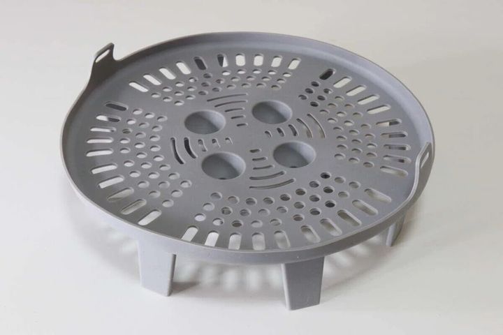 グレーの丸いシリコーン蒸し器を白背景で撮影、底に脚と穴がある