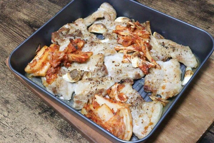 オーブントレーで焼かれた豚肉とキムチ、にんにくが盛り付けられている