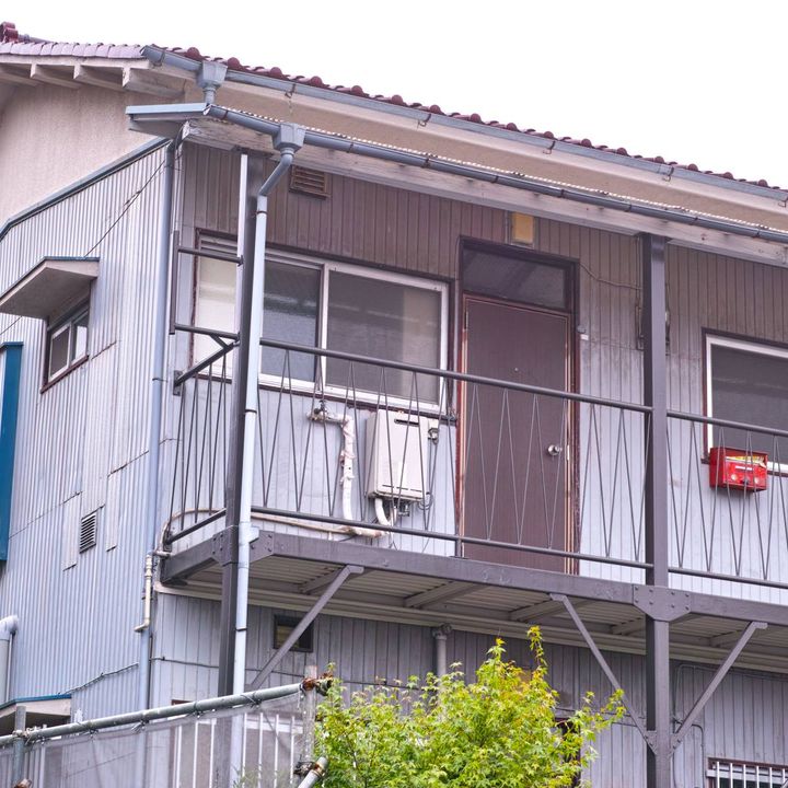 古い二階建てアパートの外観。二階の玄関ドアのそばに赤い郵便受けが設置されている。