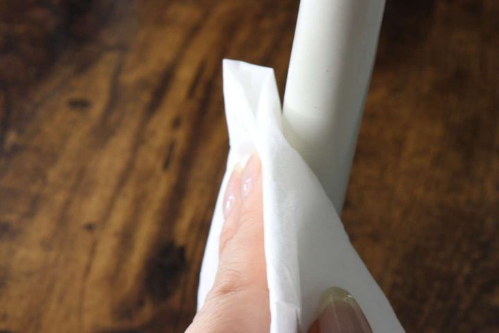 白い椅子の脚に塗布されたクリーナーを、白い布で拭き取っている手のアップ