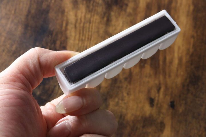 女性の手が白い洗濯ネットホルダーを持ち、裏面の黒い磁石部分を見せている