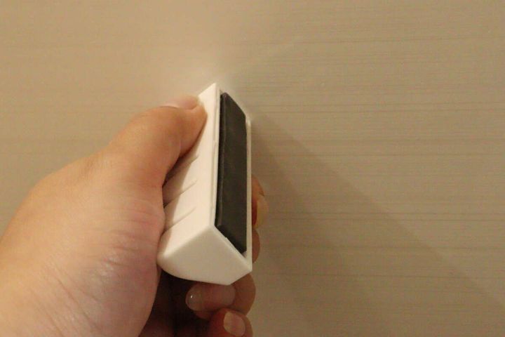女性の手が白い洗濯ネットホルダーを壁に設置しようと、磁石面を壁に当てている
