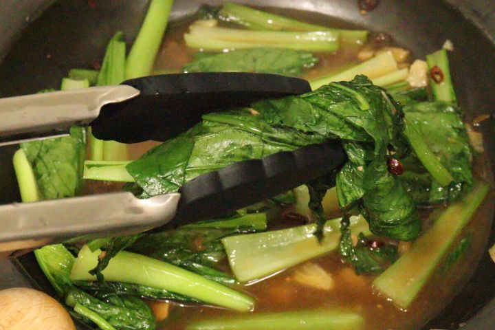 フライパンで青菜の炒め物をダイソーのシリコーントングで掴んでいる様子