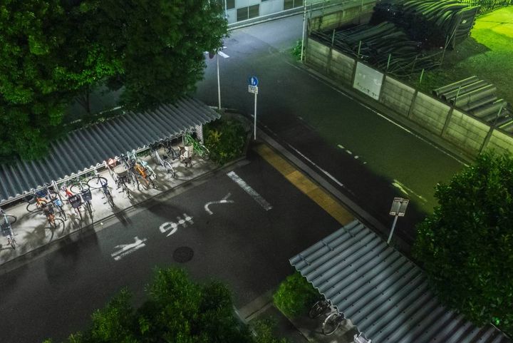 夜の屋外駐輪場を上から見下ろした風景。屋根の下に複数の自転車が並んでいる。