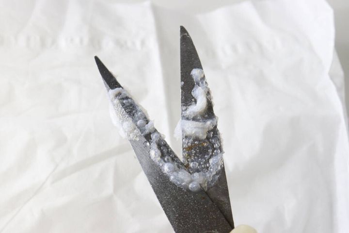 粘着汚れが付着したハサミの刃に泡状のシールはがしスプレーが噴射されている様子