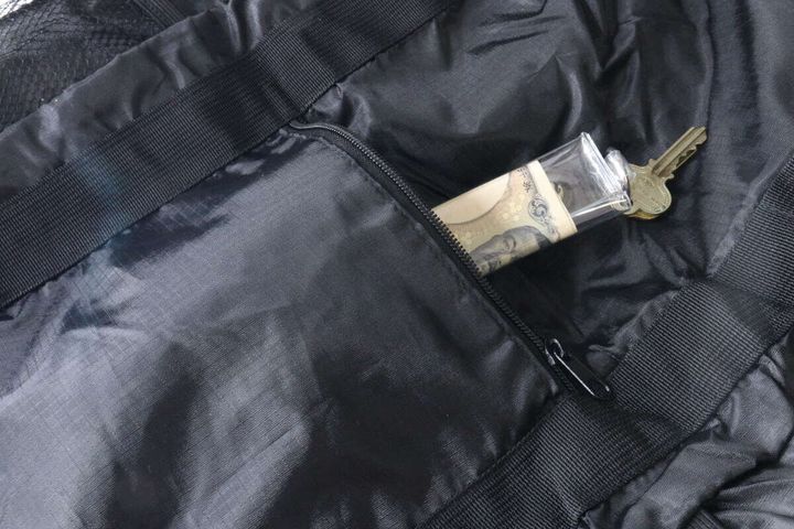 黒いトート型バックパックの前面にあるファスナーポケットに、お札と鍵が入った透明なケースが収納されている。