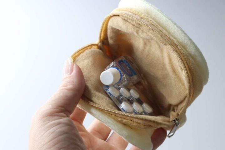 女性の指が食パン型ポーチのファスナーを開け、目薬と錠剤の薬が入っている様子
