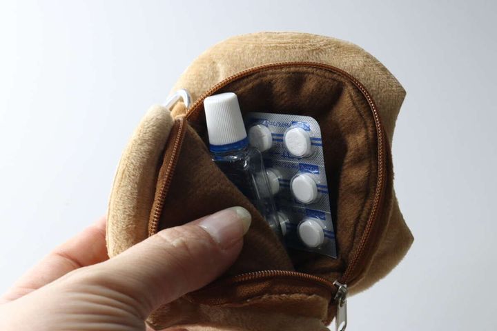 女性の指がクッキー型ポーチのファスナーを開け、目薬と錠剤の薬が入っている様子