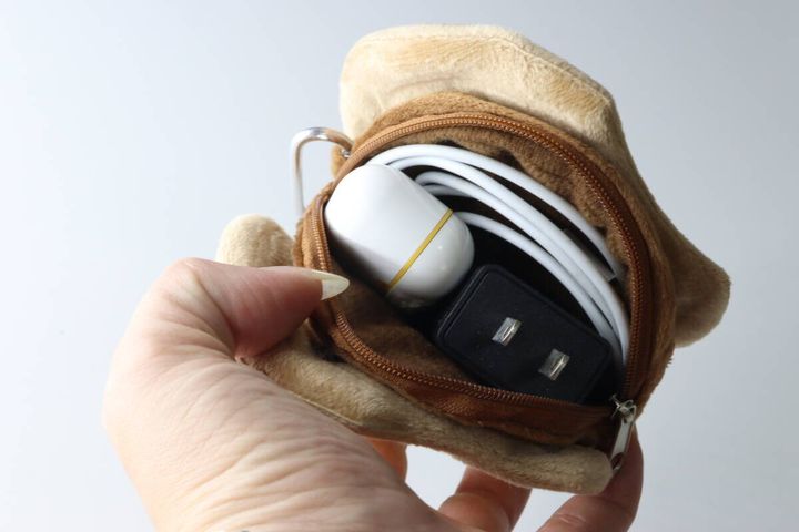 女性の指がクッキー型ポーチのファスナーを開け、ケーブル、アダプター、ワイヤレスイヤホンが入っている様子