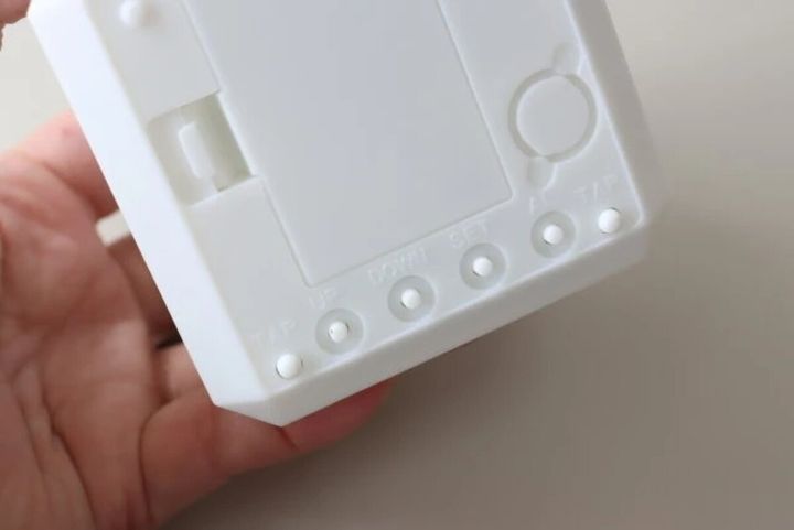 白い「7色変色ライト付デジタル時計」の底面にある設定ボタンを指で押している様子