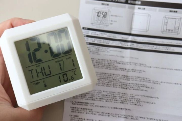 白い「7色変色ライト付デジタル時計」を手に持ち、説明書を広げた状態