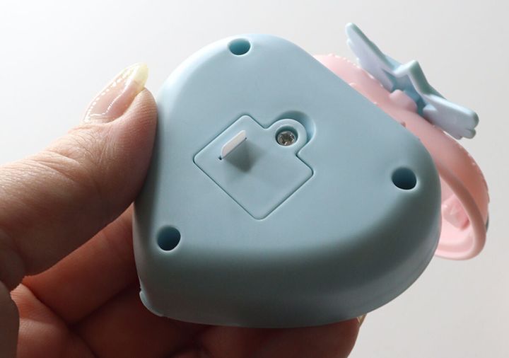 女性の手が持っているハート型コンパクトの裏面。電池カバーと絶縁シートを差し込む穴が見える