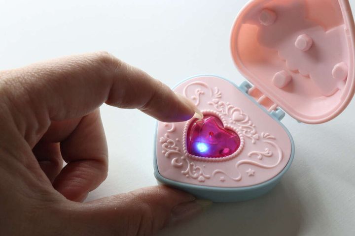 女性の指がハート型コンパクトの中央のストーンを押しており、ストーンが青く光っている