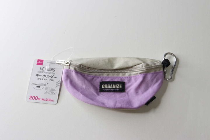 白い背景に置かれた、薄紫とベージュのウエストポーチ風キーホルダーと商品タグ