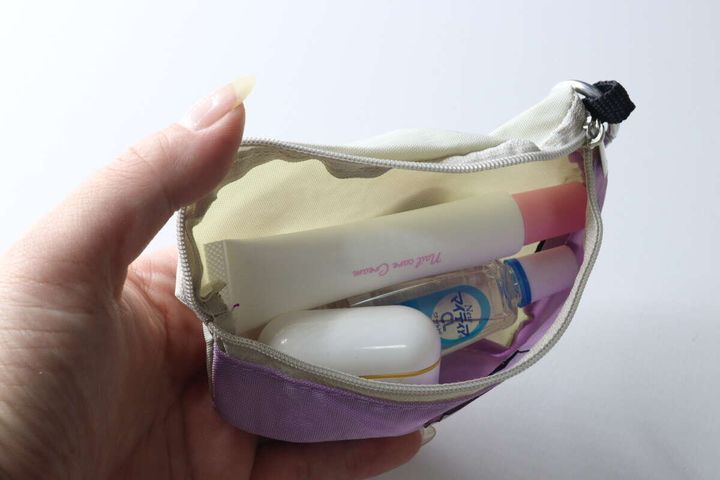女性の手が、ネイルクリームや目薬などの小物をウエストポーチ風キーホルダーに入れている様子