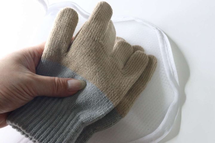 グレーとベージュの手袋を洗濯ネットに入れようとしている