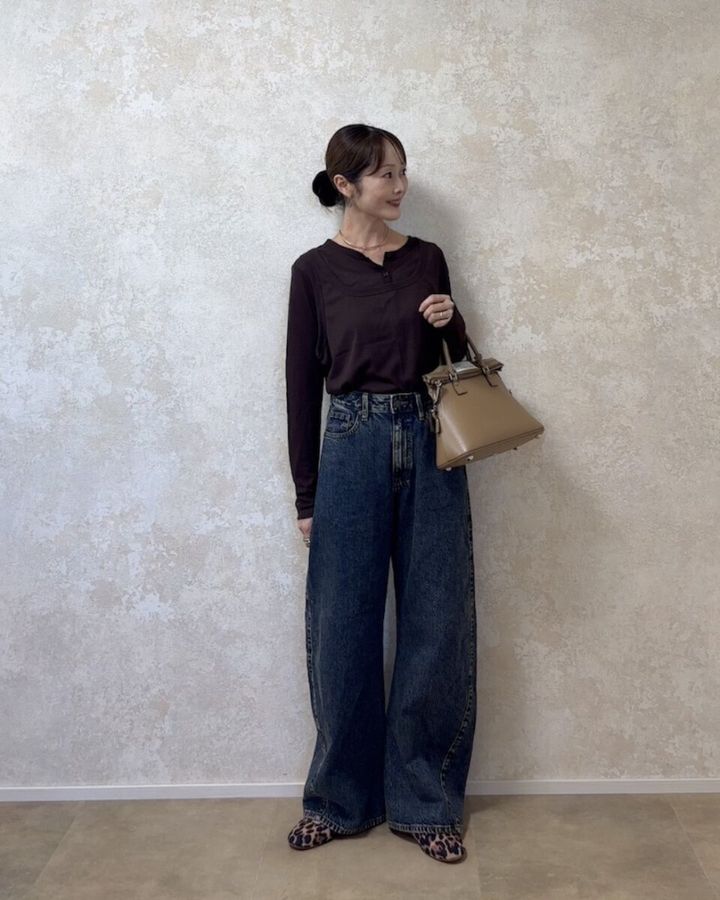 ブラウンのトップスにベージュのハンドバッグを持った大人コーデの女性