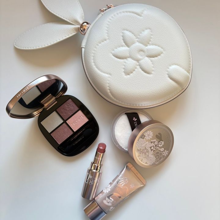 コスメデコルテの2026年ホリデー限定コフレ「メイクアップ コレクション 2026 Alice in DECORTÉ Wonderland」。白いうさぎ耳付き丸型ポーチ、4色アイシャドウパレット、リップスティック、化粧下地、フェイスパウダーの全5点が、白背景に平置きされています。