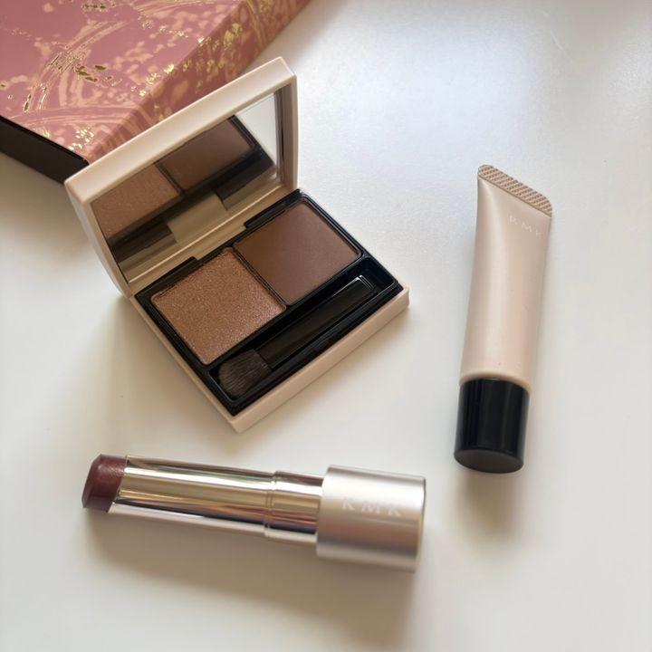 「RMK ザ クワイエット プロヴォカター キット」の全アイテムを上から撮影した写真。左上のピンクにゴールド柄の限定ボックスの手前に、開いた状態の2色アイシャドウパレット、その手前には、銀色のケースから少し繰り出したモーブトーンのリップスティック、右側には「RMK」ロゴが入った淡いベージュのチューブ型リキッドブラッシュが、白い背景に平置きされています。