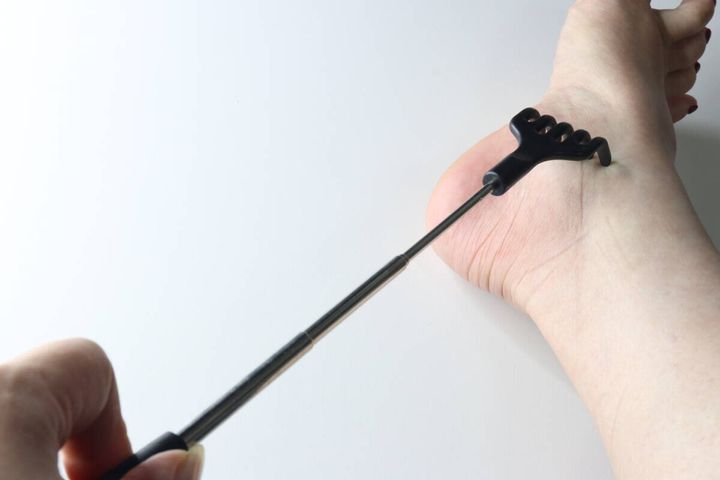 伸ばした孫の手を使って足の裏やまわりを自分でかいている様子