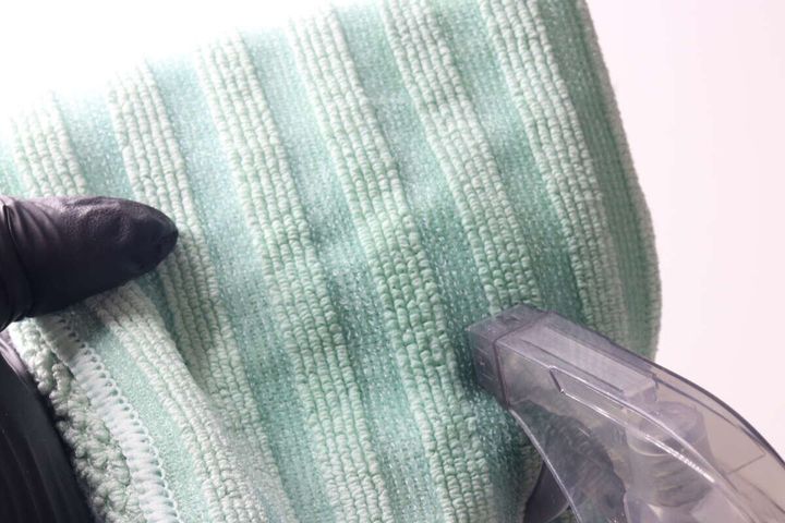 スプレー容器から緑色のマイクロファイバークロスに液を吹き付けている状態