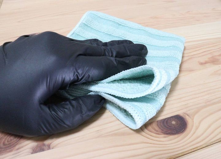 黒い手袋をつけた手で緑色のクロスを持ち木製の棚を拭いている様子