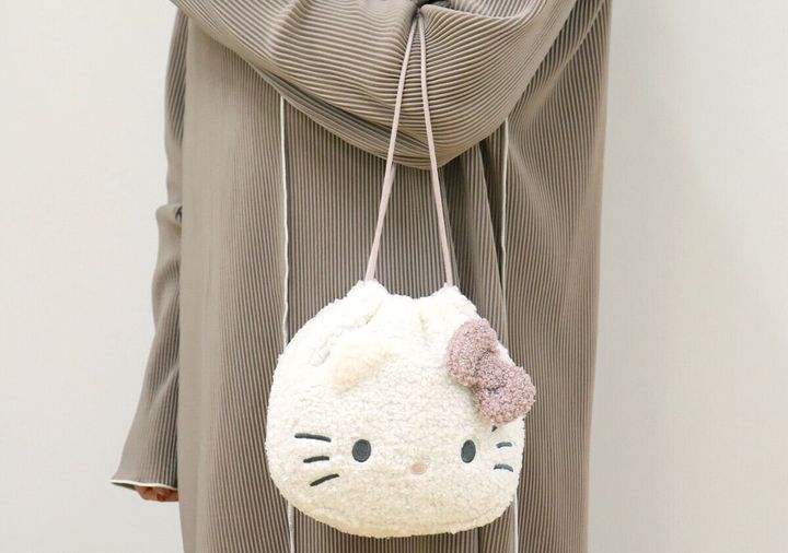 プリーツ素材の服を着た女性がハローキティポーチを肩にかけている