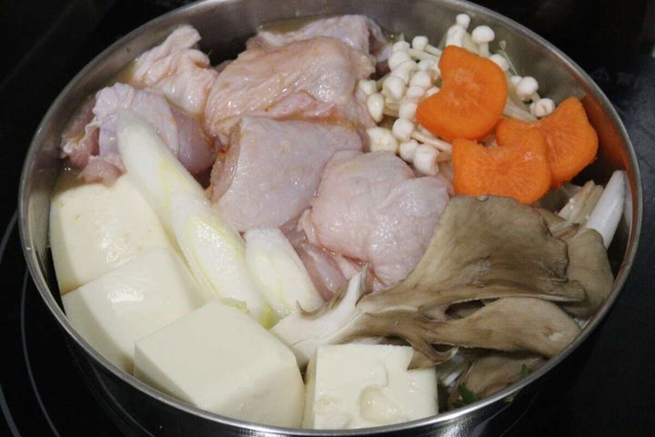 鍋に鶏肉や豆腐、きのこやにんじんなどの具材を並べた状態