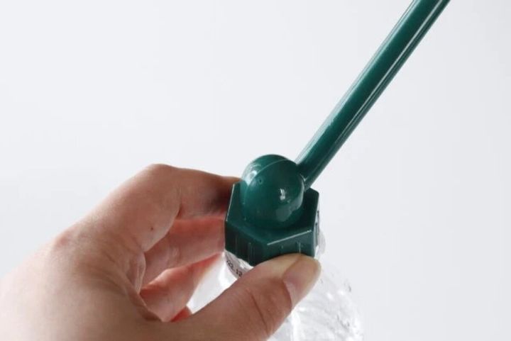 ペットボトルの口に緑色の水差しキャップを取り付けている手元