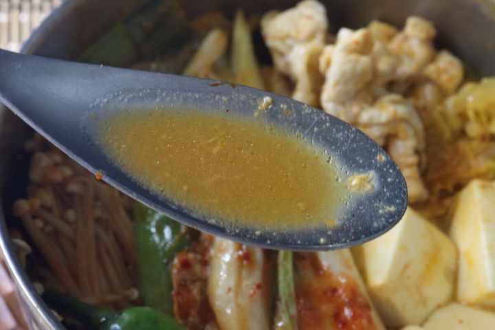 黒いスプーンですくった濃厚な味噌ベースのキムチ鍋スープ