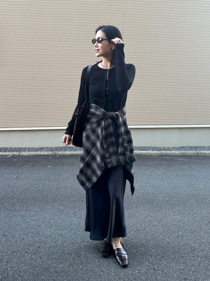 黒のカーディガンとスカートの全身黒コーデにチェックシャツを腰巻きした姿