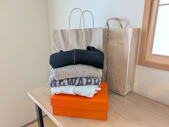 木製テーブルの上に綺麗に畳まれた洋服と紙袋が置かれている