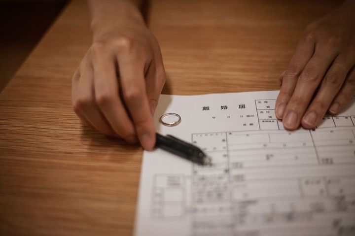 結婚指輪を外した手で、離婚届とペンを差し出している人