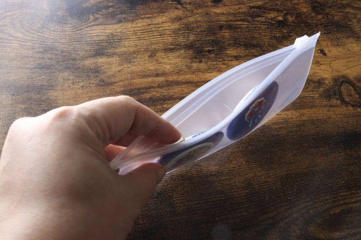 ジッパーを開けてマチのないポーチの内部に丸い缶バッジを入れている手元