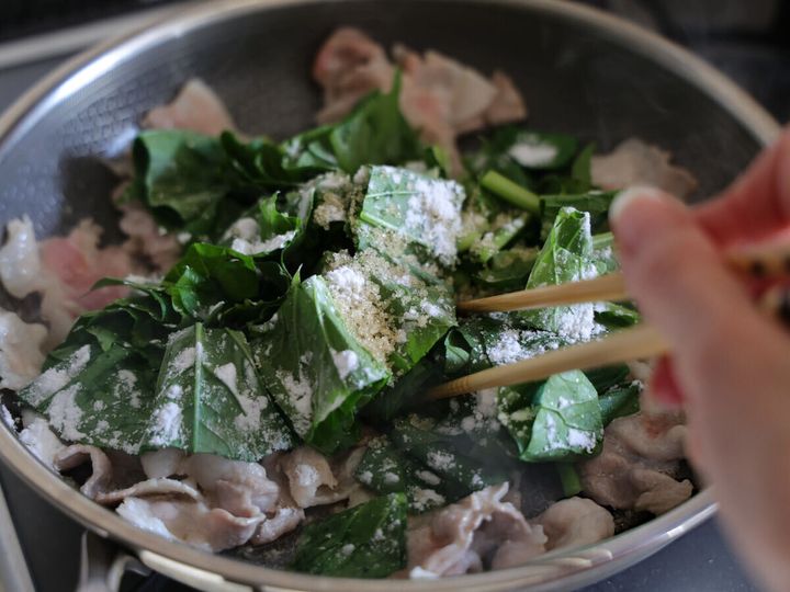 フライパンの小松菜と豚肉に砂糖と片栗粉を振りかけているところ