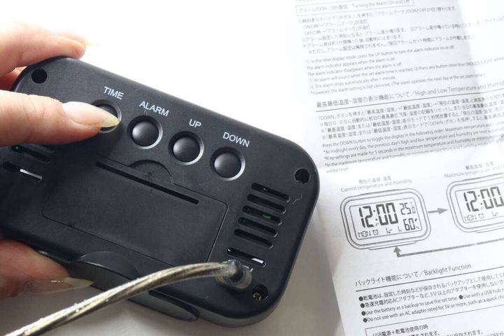 時計の裏側にあるボタンとUSB給電ケーブルの接続部分を手で支えている様子