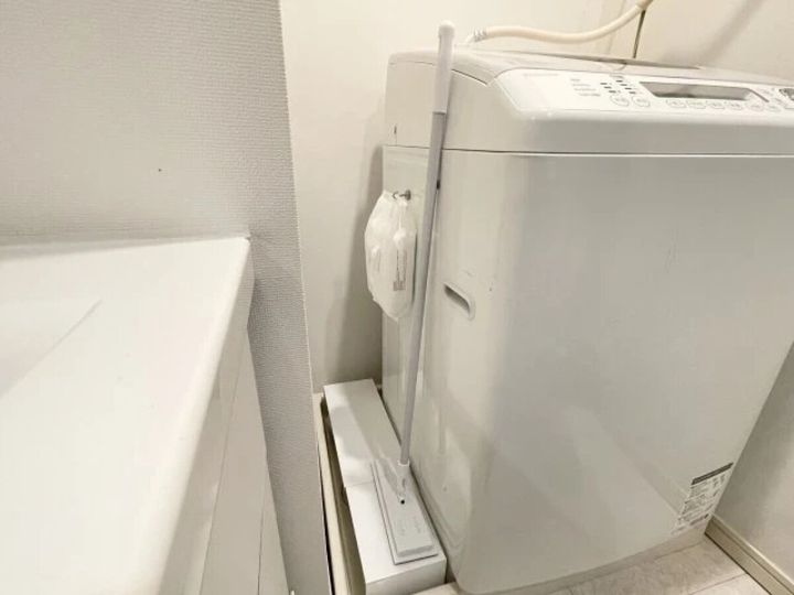 洗濯機横の狭い隙間にフローリングワイパーと掃除道具を置いている様子