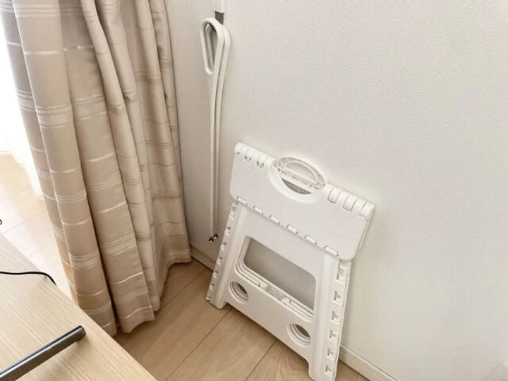 テレビボードの背面に折り畳み式のステップ台と掃除用具を立てかけている様子