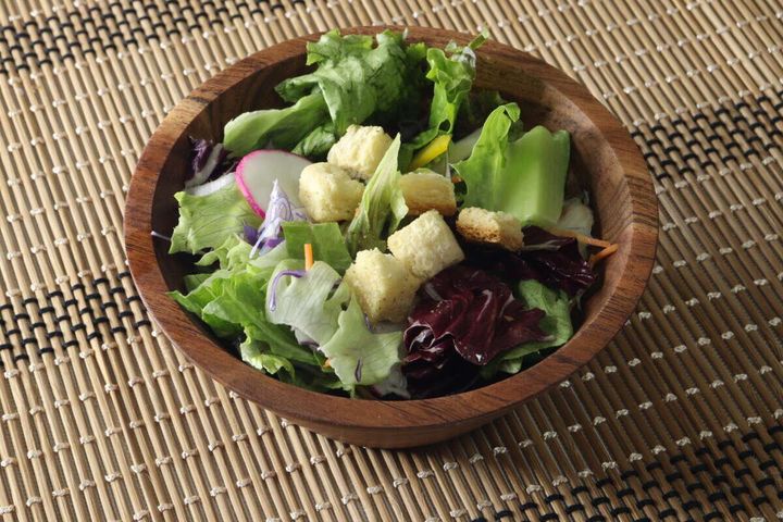 木製のボウルに入ったレタスなどのサラダにクルトンをトッピングした様子