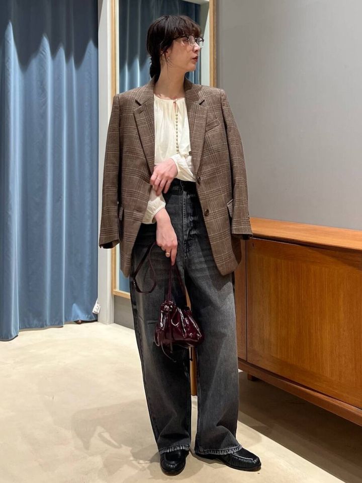 チェック柄ジャケットを肩掛けしデニムを持った女性の全身写真