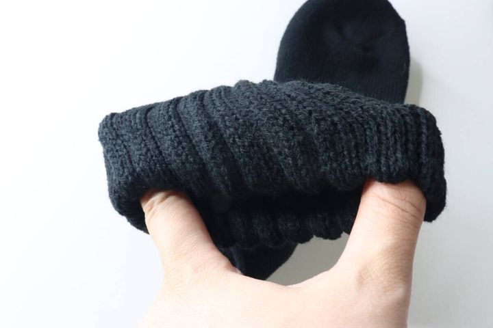 手で黒い靴下の履き口を広げ、ゆったりとした伸縮性を確認している様子。