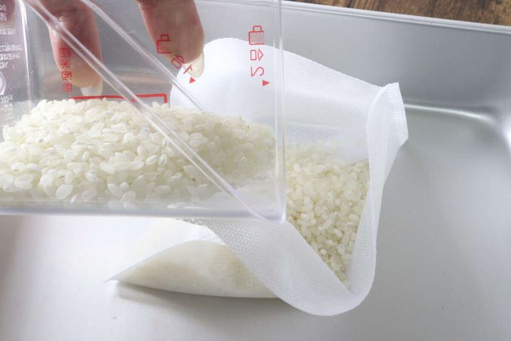 計量カップから白い生米を不織布の炊飯袋へ入れている工程