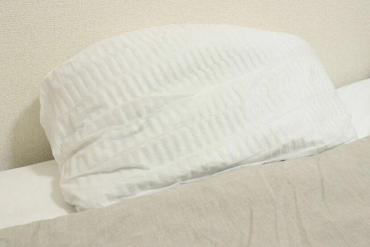 ベッドの上の枕に白い不織布まくらカバーがきれいに装着されている状態を横から撮影したもの